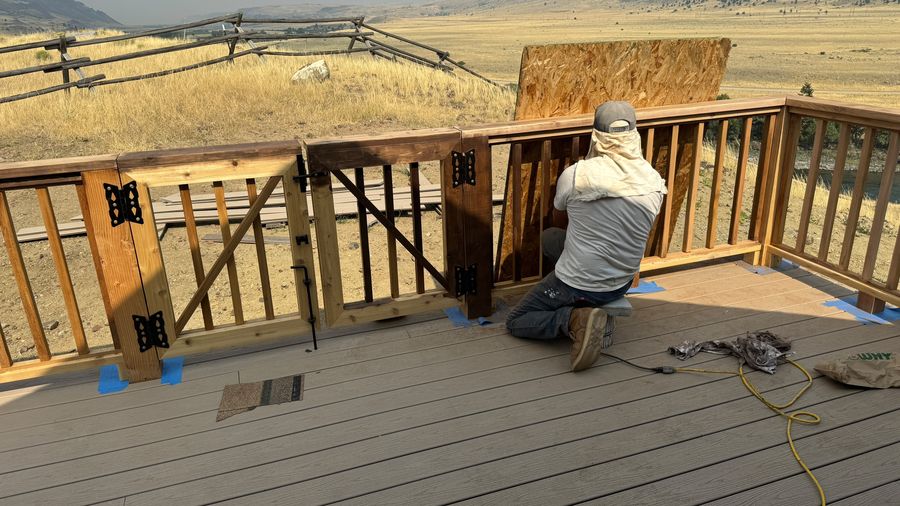 A worker staining a deck railing on a mountain deck