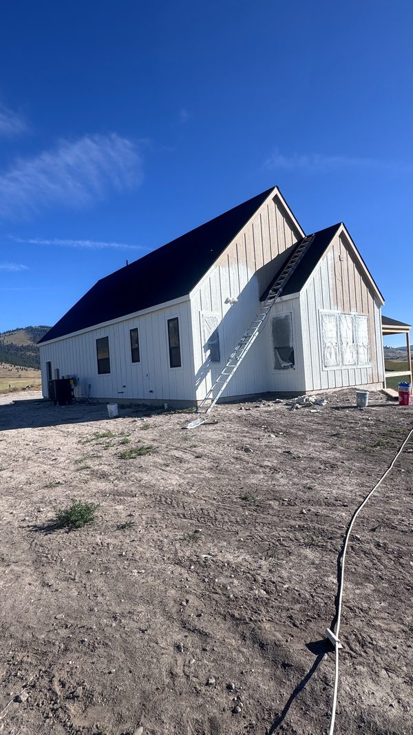 A white gabled home with a dark metal roof under a clear sky