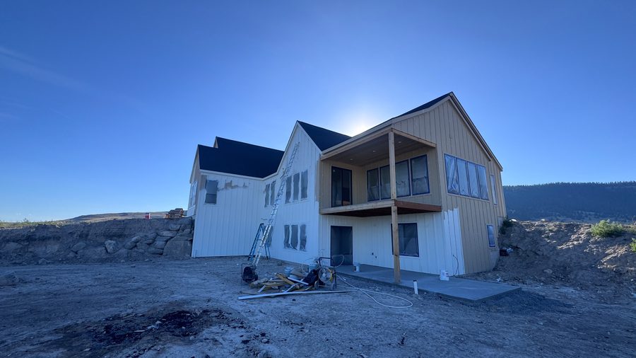 A newly built home with white and dark siding, sun behind the roofline