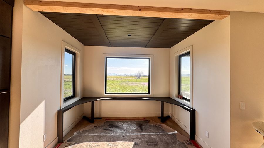 A bedroom with a dark wood ceiling and three windows