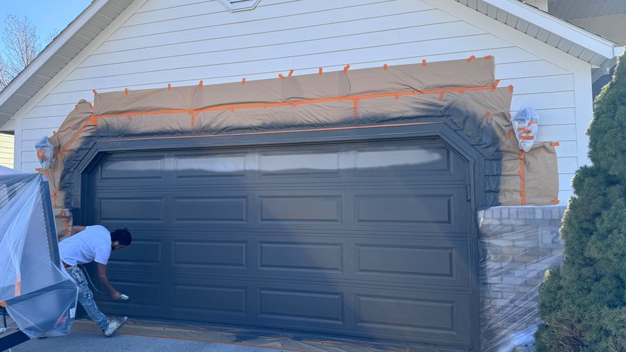 A worker masking off a garage door before paint
